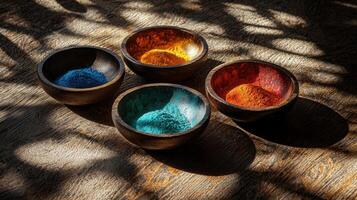 Four bowls of colored powder sitting on a wooden table photo