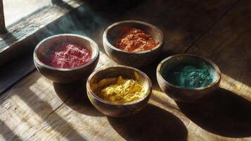 Four bowls of colored powder sit on a wooden table photo