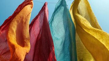 Vibrant scarves in shades of red, yellow, blue, and orange hang on a line, swaying gently in the wind against a bright blue sky, capturing a moment of warmth and color photo
