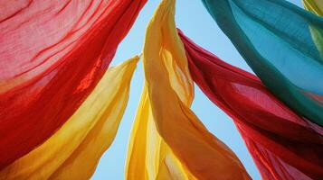 Brightly colored fabric banners in red, yellow, and blue sway gently in the breeze against a clear blue sky, creating a festive atmosphere at an outdoor event photo