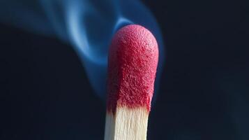 Close-up of a striking match head just after being lit, featuring a vibrant red tip and wisps of smoke rising into the dark background, highlighting the moment of ignition photo