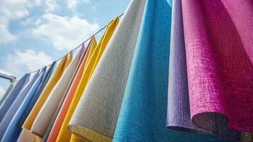 A vibrant display of various colored fabrics is seen hanging from a line. The sun illuminates the textures and hues, creating a cheerful atmosphere in an outdoor setting during the afternoon photo