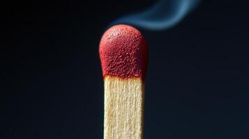 A close-up view of a matchstick igniting, with bright red head and wisps of smoke rising. The background highlights the intensity of the flame and combustion photo