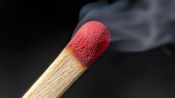 A matchstick ignites, its red tip glowing while smoke billows upwards against a dark backdrop. The detail highlights the interplay of fire and smoke photo