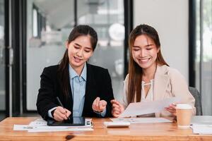 Two women engaged in a collaborative business meeting, discussing documents and using a digital tablet in a modern office environment. photo
