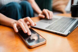 Hands interacting with a laptop and smartphone on a wooden table, depicting modern technology use in a home environment. photo