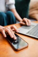 Hands interacting with smartphone and laptop, showcasing multitasking and remote work in a cozy setting. photo