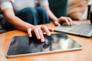 Hands interacting with a tablet and laptop on a wooden table, showcasing modern technology use in a home setting. photo