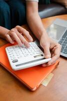 Hands calculating finances on an orange notebook beside a laptop, symbolizing budgeting and financial planning. photo