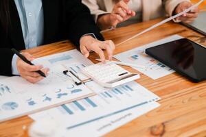 Close-up of hands using a calculator with financial charts and graphs on a wooden desk during a business meeting. photo