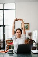 Woman enjoying a stretch at her home office desk, surrounded by a cozy and modern interior with a laptop and coffee. photo