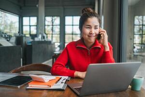 Businesswoman multitasking with laptop and phone in a bright, modern office space, showcasing remote work and technology. photo