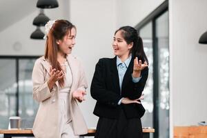 Two businesswomen in a modern office, smiling and talking, showcasing teamwork and communication. photo