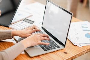 Hands typing on a laptop with financial documents and a calculator on a wooden desk, depicting a modern office environment. photo