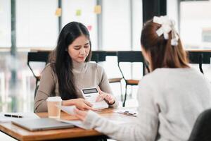Two women working together in a modern office, using a calculator and reviewing documents over coffee. photo