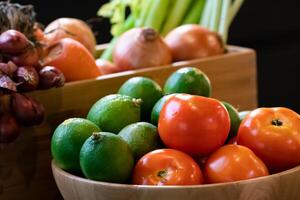 Vegetable tomato and lime in wood bowl with blur background carrot, onion, and red shallot in wood box. All are in studio light. photo