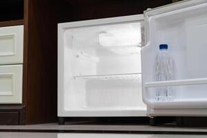 mini fridge in low angle view, inside it is empty shelves placed under wooden counter and next to wood closet photo