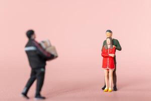 Miniature figurine scene depicting a man carrying presents towards a couple, with the woman appearing surprised, valentine concept photo