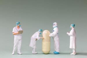 Tiny figurines of doctors and scientists examining an oversized medical capsule photo