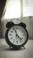 Timelapse of Black alarm clock in house with curtain background and soft sunlight, vintage style. Time moves quickly, working hours, and management time concept, Footage vertical video
