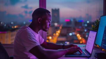 A focused individual is seated at a desk using a laptop while working at night. The backdrop displays a colorful city skyline illuminated by city lights, creating a lively atmosphere. photo