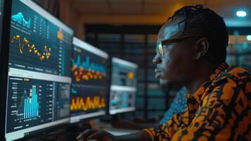 A data analyst focuses on various digital displays filled with vibrant graphs and statistics in a contemporary office setting. The atmosphere is illuminated, suggesting late night work. photo