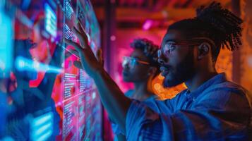 Two individuals focus intently on a digital display, interacting with data in a modern technology lab filled with colorful lighting, creating a dynamic atmosphere. photo