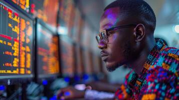 A dedicated individual wearing glasses concentrates intently on financial data displayed across several monitors, surrounded by a high tech workspace illuminated by screen lights. photo