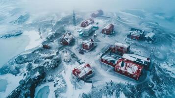 Snow covers the ground and rooftops of a remote settlement marked by red buildings. The cloudy sky enhances the tranquil winter atmosphere, creating a serene scene. photo