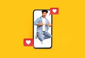 A person is joyfully jumping while holding a smartphone, displaying text messages related to love and social media interactions. The vibrant yellow background enhances the cheerful mood. photo