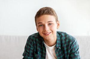 Cheerful teenager guy sitting on sofa at home, talking on camera, shooting for his followers, free space photo