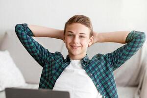 Happy smart school boy sitting in front of laptop, making report at home photo