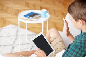 Boy waving to digital tablet with empty screen, using application for videcall, home interior photo