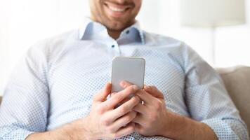 Browsing Internet. Cheerful handsome man using his smartphone sitting on the couch at home, copyspace photo