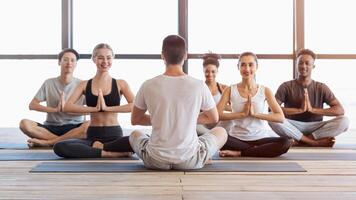 International group of young people attending yoga class in modern studio, meditating with coach in lotus position photo