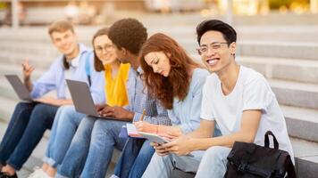 Teamwork Concept. Multiethnic students sitting on steps and learning, asian boy looking at camera photo