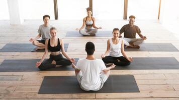 Group of young people having yoga class with coach in studio, sitting in lotus position and smiling, copy space photo