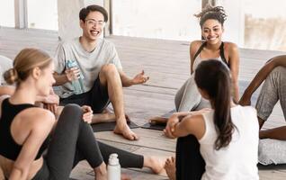 Group of diverse young people communicating before yoga class in studio, sitting on floor and chatting photo