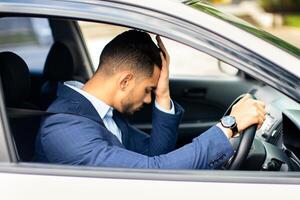 Car accident concept. Upset arab businessman driver sitting at front seat and touching his head, having automobile crash. Middle-eastern guy getting late for flight, got stuck in traffic, side view photo