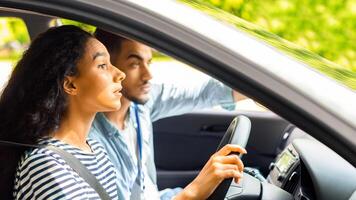 Nervous young lady driving school student driving car with instructor, making mistakes or failed exam, exhausted coach arab guy sitting by with chart and pointing at road, side view, copy space photo