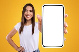 Mobile App Advertisement. Excited Woman Showing White Empty Smartphone Screen Recommending App Posing Over Orange Studio Background, Smiling To Camera. Check This Out, Cellphone Display Mock Up photo