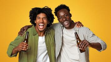 Portrait Of Two Happy Black Friends Embracing And Holding Bottles With Beer, Cheerful African American Guys Having Fun While Posing Together Over Beige Background In Studio, Enjoying Party photo