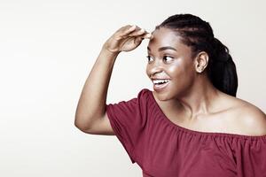 Curious african american young woman looking at something interesting or exciting, holding hand by forehead and looking at copy space for advertisement, beige studio background, panorama photo