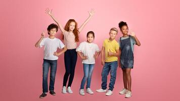 Full length portrait of happy diverse schoolkids making different gestures over pink background photo