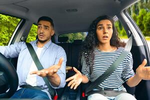 Indignant middle-eastern young couple having car accident or got stuck in traffic while travelling, sitting inside automobile, looking at road, gesturing and resenting, shot from auto dashboard photo