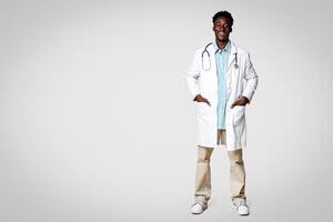 Portrait Of Smiling Young African American Doctor Wearing Uniform And Stethoscope Standing Over Beige Background In Studio, Black Male Medical Looking And Smiling At Camera, Full Length, Copy Space photo