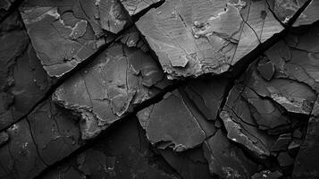 Dark slate surface exhibits intricate cracks and layers, revealing geological history and natural wear. The texture creates a striking visual contrast and depth. photo