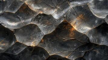 A close up of a dark rock surface reveals unique textures and patterns that are enhanced by natural light, emphasizing the mineral formations and geological details present in the material. photo