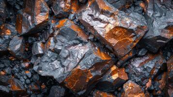 Natural minerals with dark tones and striking orange highlights are closely packed together, showcasing sharp angles and intricate textures under soft lighting. photo