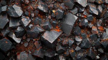 A collection of dark volcanic rocks with angular shapes and textured surfaces, speckled with hints of orange, set against a gritty background of smaller stones and minerals. photo